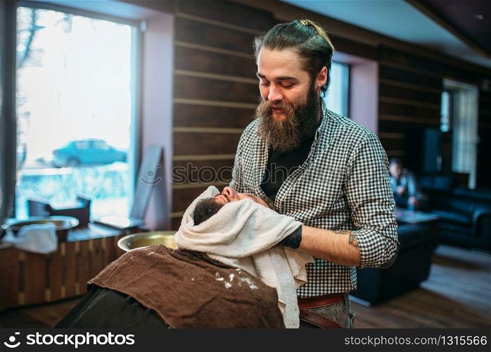 Barber wiping the client beard with a towel, barbershop interior on background.