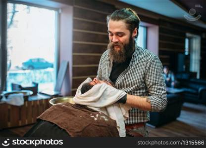 Barber wiping the client beard with a towel, barbershop interior on background.