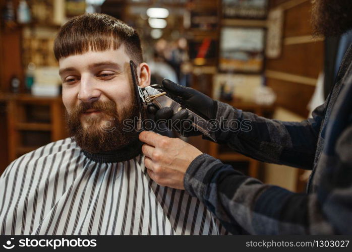 Barber with comb and electric clipper makes a haircut to a client. Professional barbershop is a trendy occupation. Male hairdresser and customer in retro style hair salon. Barber with comb and clipper makes a haircut