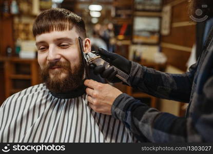 Barber with comb and electric clipper makes a haircut to a client. Professional barbershop is a trendy occupation. Male hairdresser and customer in retro style hair salon. Barber with comb and clipper makes a haircut