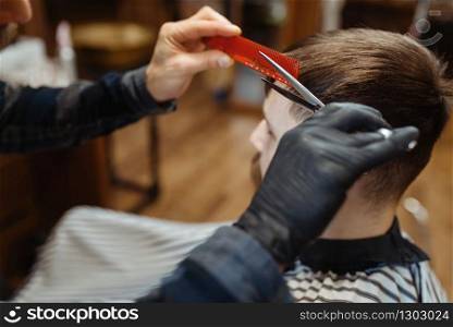 Barber with comb and scissors makes a haircut to a client. Professional barbershop is a trendy occupation. Male hairdresser and customer in retro style hair salon. Barber with comb and scissors makes a haircut