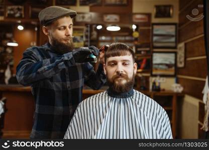 Barber with comb and scissors makes a haircut to a client. Professional barbershop is a trendy occupation. Male hairdresser and customer in retro style hair salon. Barber with comb and scissors makes a haircut