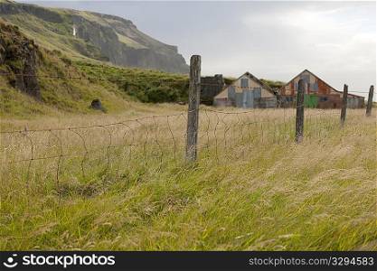 Barbwire fence and fenceposts in a pasture with barns and mountains