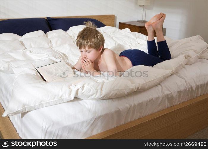Bare chested boy laying on bed in bedroom reading book