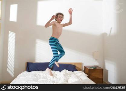 Bare chested boy playing and jumping in mid-air on bed in bedroom
