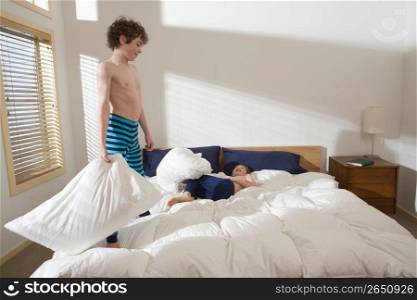 Bare chested brothers rough housing and pillow fighting on bed in bedroom
