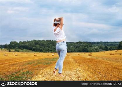 barefoot girl in straw hat stands on a haystack on a bale in the agricultural field after harvesting.. girl in straw hat stands on a haystack on a bale in the agricultural field after harvesting
