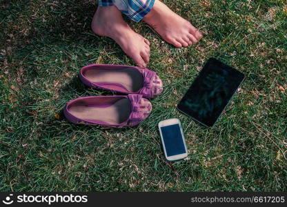 Barefoot girl relaxing on grass with tablet-pc and smartphone. Barefoot girl sitting on grass with tablet-pc and smartphone