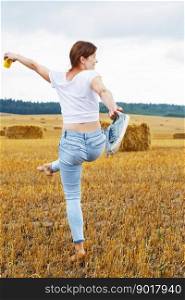 barefoot girl with sneakers and cardboard cup with coffee in hand walking in the agricultural field with haystack and bales after harvesting.. barefoot girl with sneakers and cardboard cup with coffee in hand walking in the agricultural field