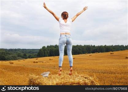 barefoot girl with straw hat stands on a haystack on a bale in the agricultural field after harvesting.. girl with straw hat stands on a haystack on a bale in the agricultural field after harvesting