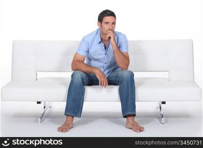barefoot man sitting on a modern couch and wondering