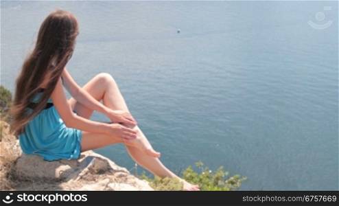 barefoot young woman resting on top of a mountain by the sea