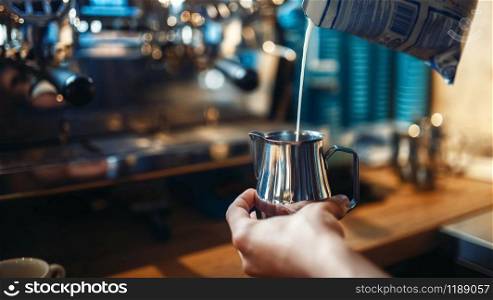 Barista in apron pours cream into the cup of coffee, cafe counter on background. Professional cappuccino preparation by bartender. Barista pours cream into the cup of coffee