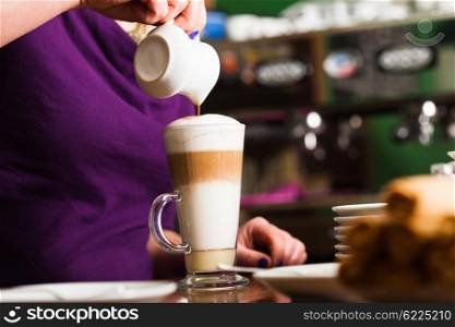 Barista is pouring coffee in milk - preparing coffe latte. Barista is preparing latte