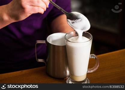Barista is pouring milk foam in to a glass with caramel - preparing sweet and spicy coffee latte. Barista is preparing latte