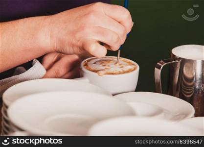 Barista is show how to make latte art coffee. Lesson with special metal device - latte-art pen tool.. Latte art on the cup