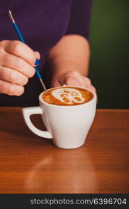 Barista making a cup of latte art coffee with special metal device - latte-art pen tool. Latte art on the cup