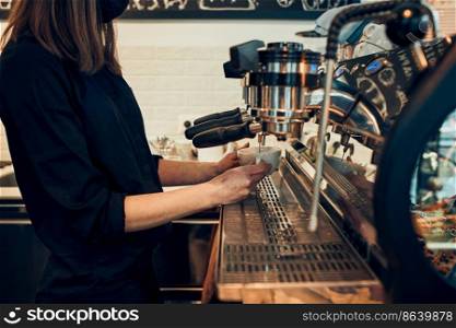 Barista making coffee pouring coffee to a cup making coffee using a coffee maker. Woman bartender making espresso, preparing coffee drink. Young woman working in a coffee shop