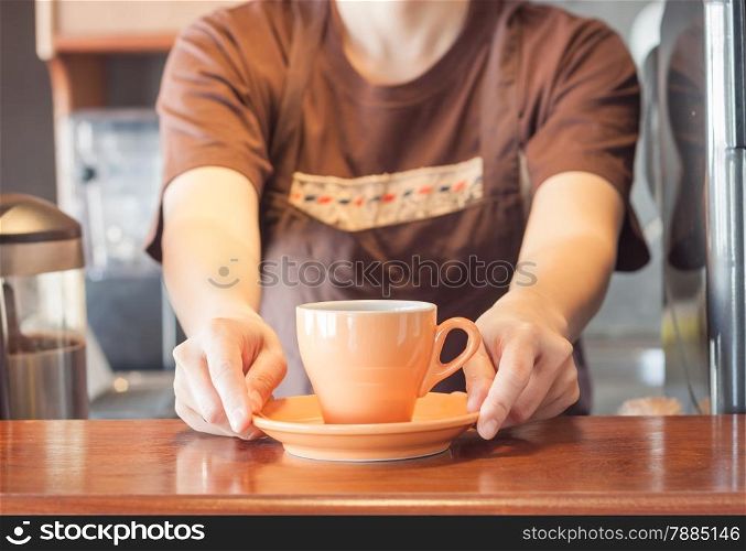 Barista offering orange cup of coffee, stock photo