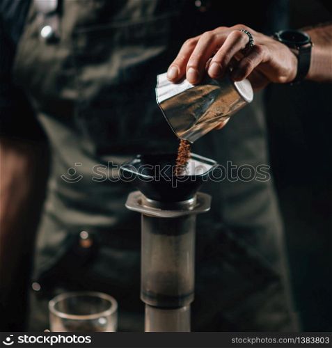 Barista pouring coffee into air press coffee maker. Barista with tattooed arms wearing dark uniform.