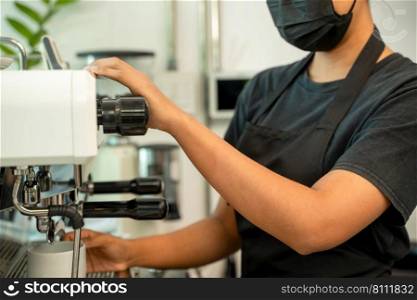 Barista prepares coffee while working during the coronavirus pandemic and wearing a protective mask.