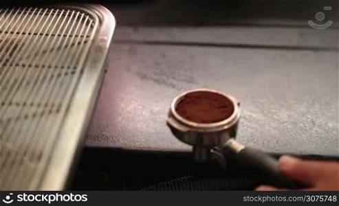 Barista using a tamper to press ground coffee into a portafilter. Woman using professional tools for coffee preparation in a cafe