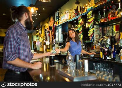 Barmaid handing change to male customer in public house