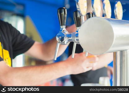 Barman hand at beer tap pouring a draught lager beer serving in a restaurant or pub.