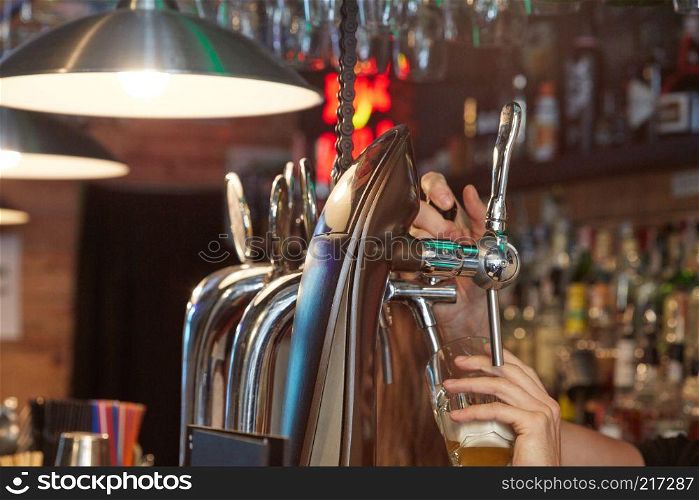 Barman hands pouring a lager beer in a glass.. Barman pouring beer