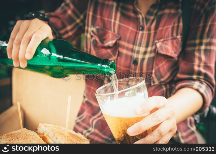 Barman holding bottle beer and pouring in mug.