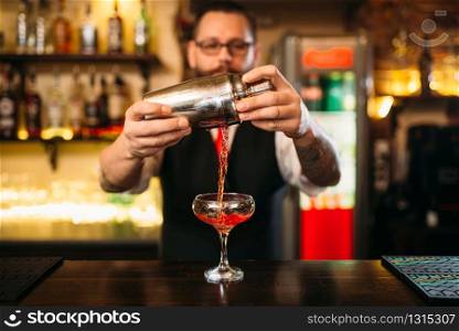Barman is making alcohol cocktail at bar counter. Barman with shaker and glass of beverage