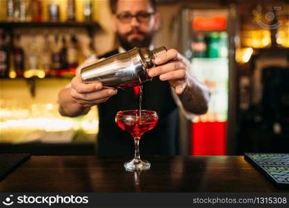 Barman is making alcohol cocktail at bar counter. Barman with shaker and glass of beverage. Barman is making alcohol cocktail at counter