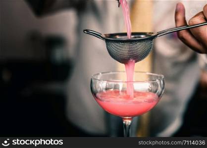 Barman is making pink cocktail at night club.
