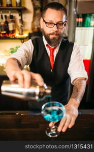 Barman with shaker making alcohol cocktail behind a bar counter