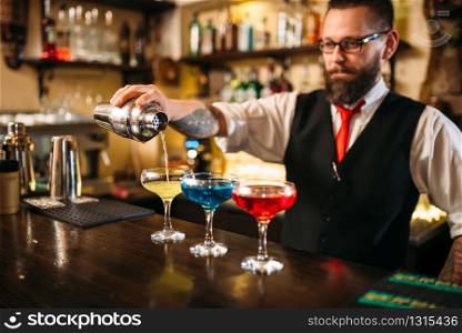 Barman with shaker making alcohol cocktails behind a bar counter in nightclub