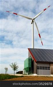 barn covered with solar panels and wind turbine in the background