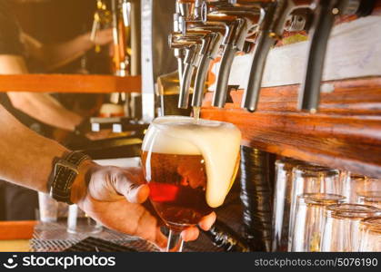 Bartender hand pouring draught beer to glass from a pub tap. Barman is serving beer from faucet