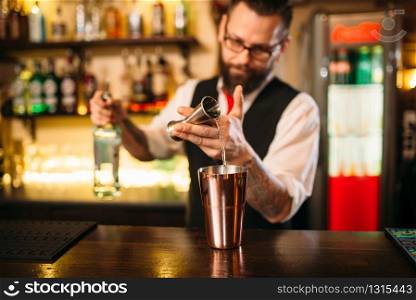 Bartender pouring alcohol beverage in metal glass at restaurant