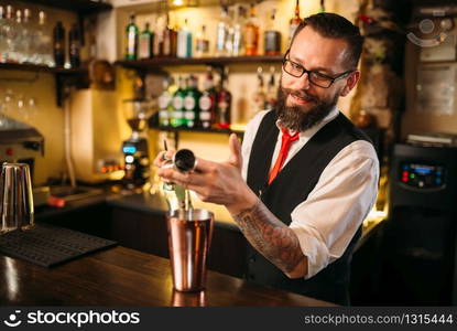 Bartender pouring alcohol beverage in metal glass at restaurant. Bartender pouring alcohol beverage in metal glass