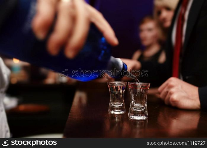 Bartender pouring strong alcoholic drink into small glasses on bar, shots in a nightclub or bar.. Bartender pouring strong alcoholic drink into small glasses on bar, shots in a nightclub or bar
