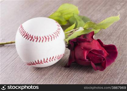 Baseball near a red rose over wooden background, horizontal image