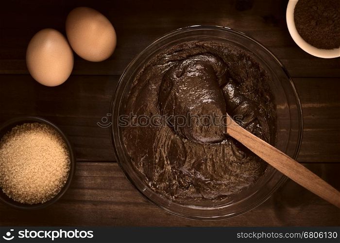 Basic brownie, chocolate cake or cookie dough in glass bowl with ingredients on the side, photographed overhead on dark wood with natural light (Selective Focus, Focus on the top of the dough)