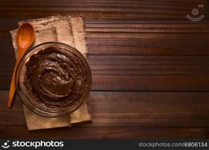 Basic brownie, chocolate cake or cookie dough in glass bowl with wooden spoon on the side, photographed overhead on dark wood with natural light (Selective Focus, Focus on the top of the dough)