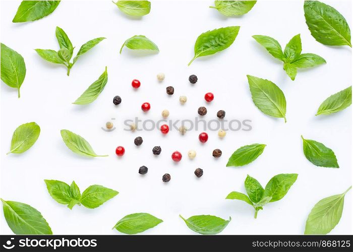 Basil leaves with different type of peppercorns on white background. Top view