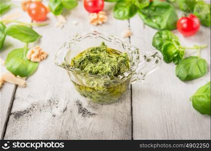 basil pesto in glass cup over tomatoes, walnut and parmesan on white wooden background
