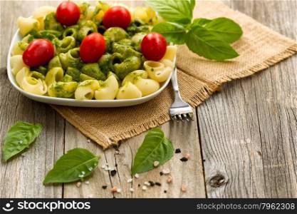 Basil pesto with shell shaped pasta and cherry tomatoes. Selective focus on front part of plate.