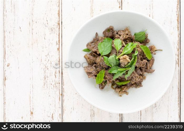 basil stir fried beef in white ceramic plate on white old wood texture background with copy space for text, top view, flat lay, Pad Ka Prao Neua, Thai food