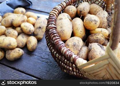 Basket full of fresh, young potatoes , towel and knife on wooden background, top view .. Basket full of fresh, young potatoes , towel and knife on wooden background, top view