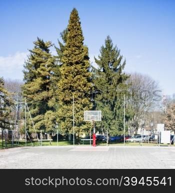 Basket in a playground, with big trees on the back, horizontal image