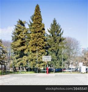 Basket in a playground, with big trees on the back, horizontal image